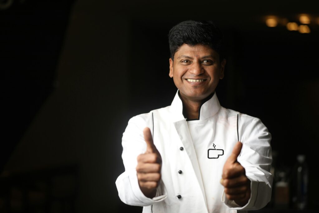 A cheerful chef in a white uniform giving a thumbs up, capturing the spirit of hospitality in Bengaluru.