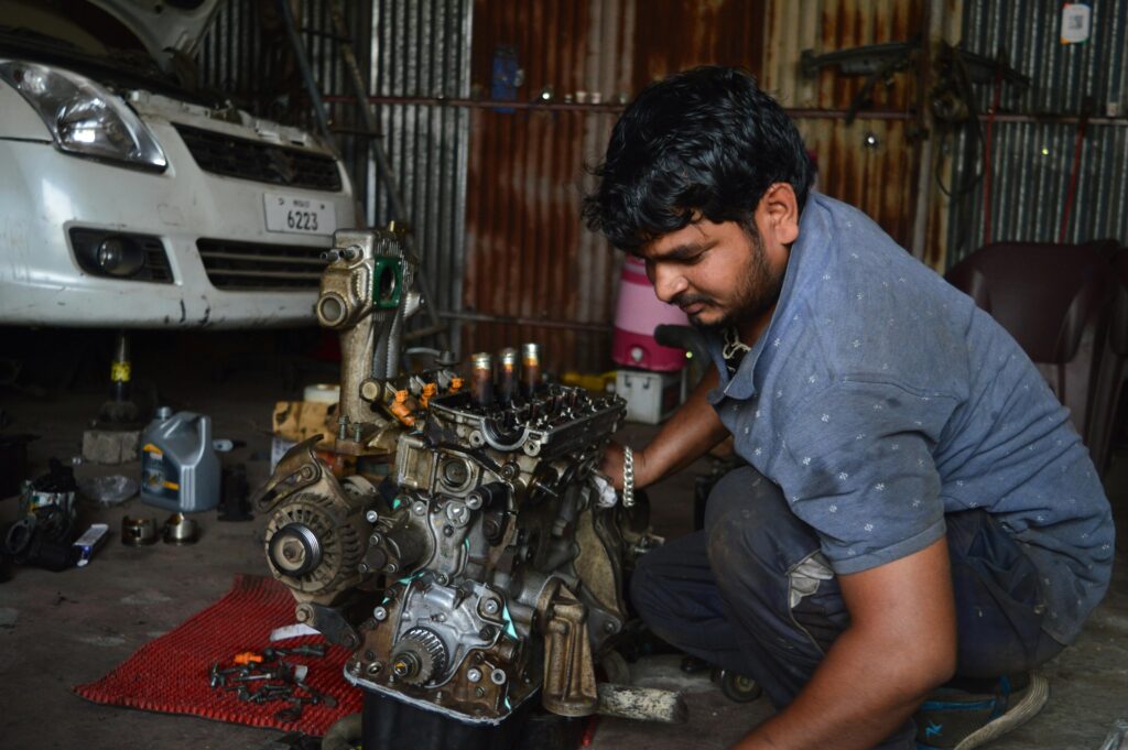 A mechanic works on an engine in a garage in India, showcasing auto repair skills.